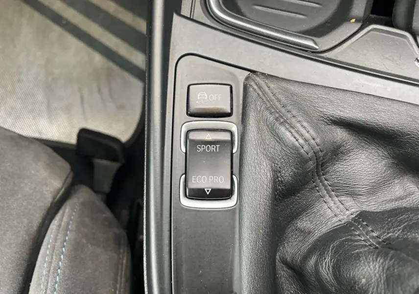 Gros plan sur la console centrale de la BMW Série 2 Coupé F22 blanche, montrant les boutons mode Sport et Eco Pro près du levier de vitesse cuir.