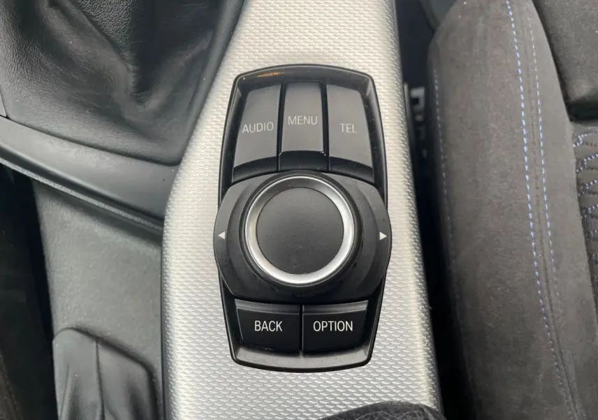 Gros plan sur la molette de commande iDrive noire et argentée au centre de la console d'une BMW Série 2 Coupé blanche.