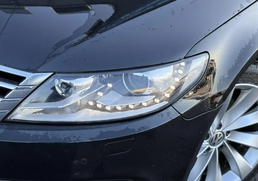 Gros plan sur le phare avant droit et la jante alliage 18'' argentée d'une Volkswagen Passat CC Deep Black 2015.