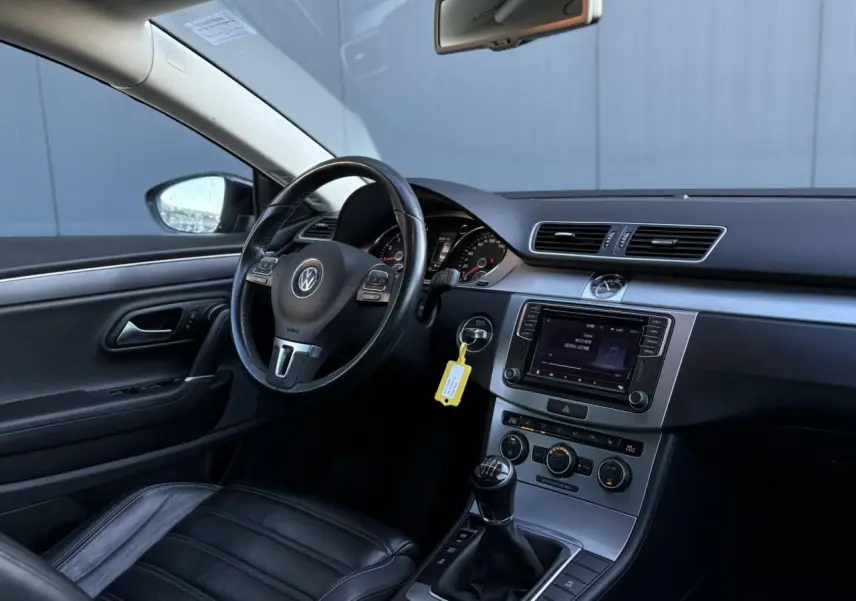 Vue intérieure côté conducteur de la Volkswagen Passat CC 1.4 TSI 2015 avec sellerie cuir noire et tableau de bord moderne.
