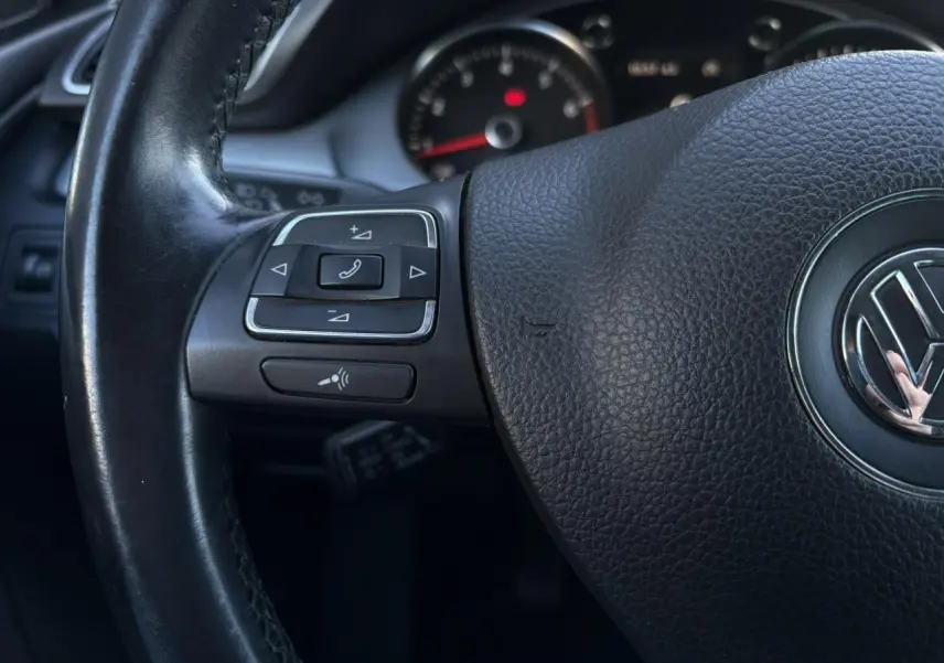 Gros plan sur le volant cuir multifonction noir de la Volkswagen Passat CC 2015 avec commandes intégrées.