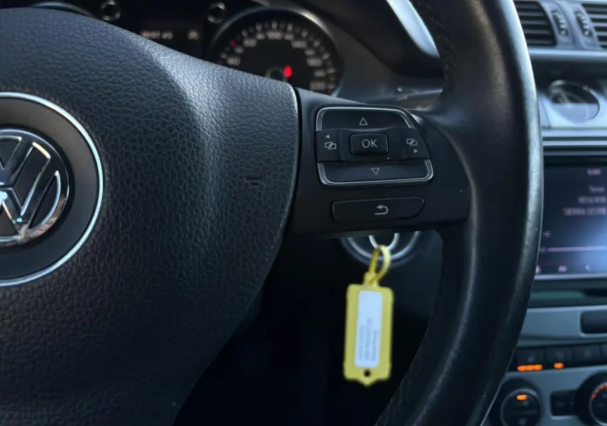 Gros plan sur le volant cuir multifonction de la Volkswagen Passat CC 1.4 TSI, avec commandes intégrées et tableau de bord en arrière-plan.