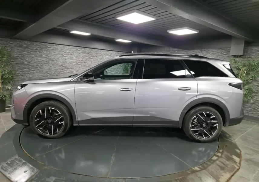 Vue de profil côté gauche d’un Peugeot 5008 gris métallisé avec jantes alliage noires dans un showroom.