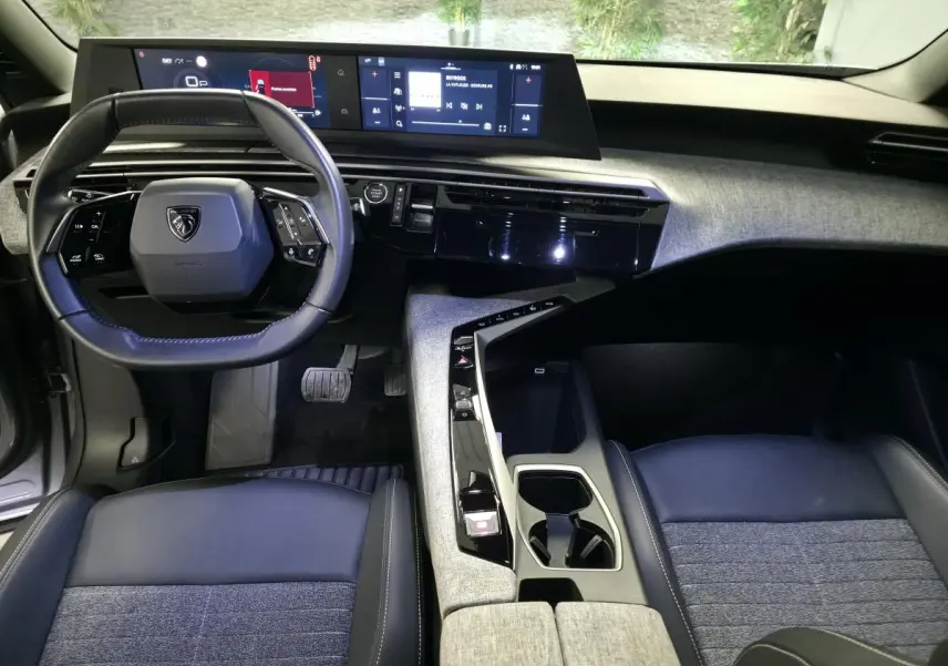 Vue intérieure avant du Peugeot 5008 2025 hybride, tableau de bord avec double écran et volant compact cuir noir.