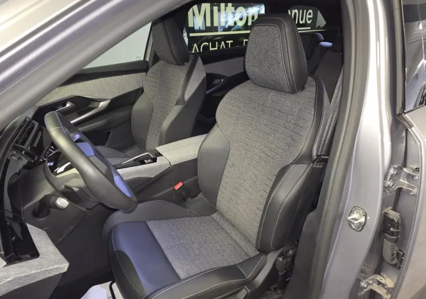 Vue intérieure côté conducteur du Peugeot 5008 gris 2025, mettant en valeur les sièges tissu et cuir avec surpiqûres contrastées.