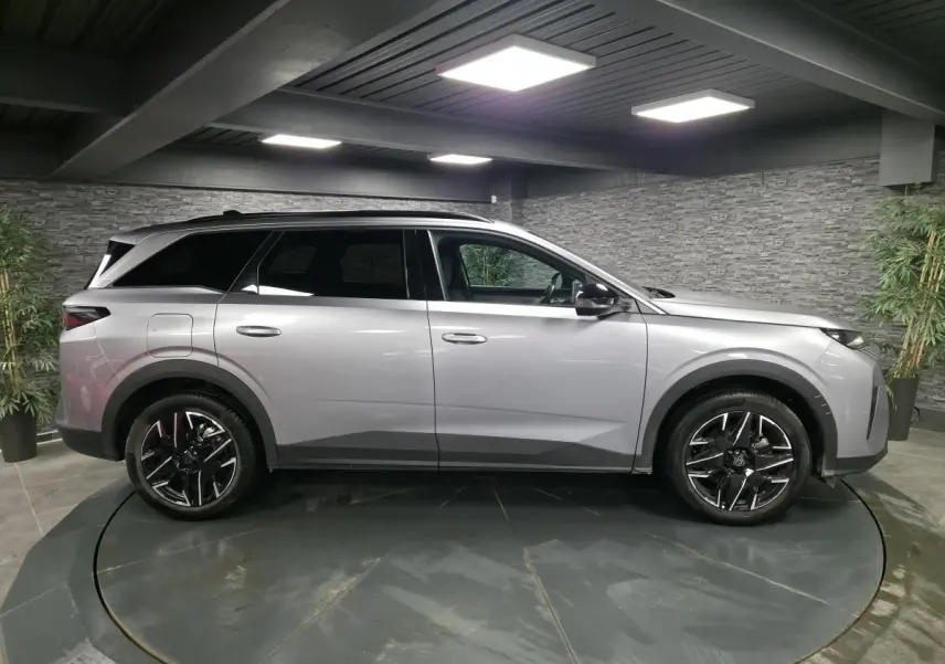 Vue de profil côté gauche d'un Peugeot 5008 gris métallisé avec jantes alliage noires diamantées dans un showroom.