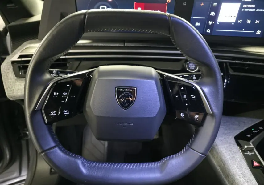 Volant cuir noir au design compact avec logo Peugeot, vue frontale de l'habitacle du 5008 hybride gris 2025.