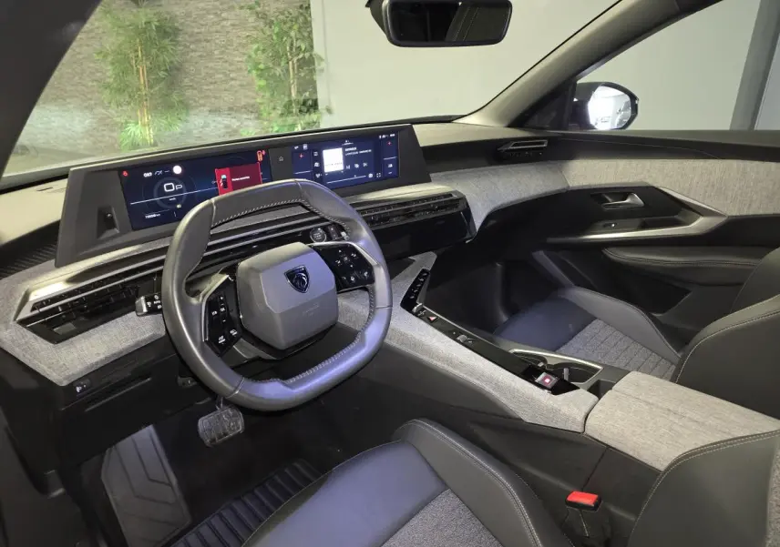 Vue intérieure côté conducteur du Peugeot 5008 gris 2025, avec tableau de bord numérique panoramique et volant compact cuir noir.