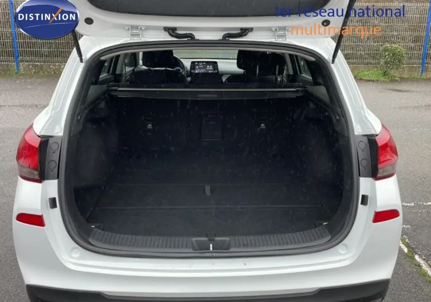 Vue arrière ouverte sur le coffre spacieux d’une Hyundai i30 SW blanche polaire, avec intérieur sombre visible.
