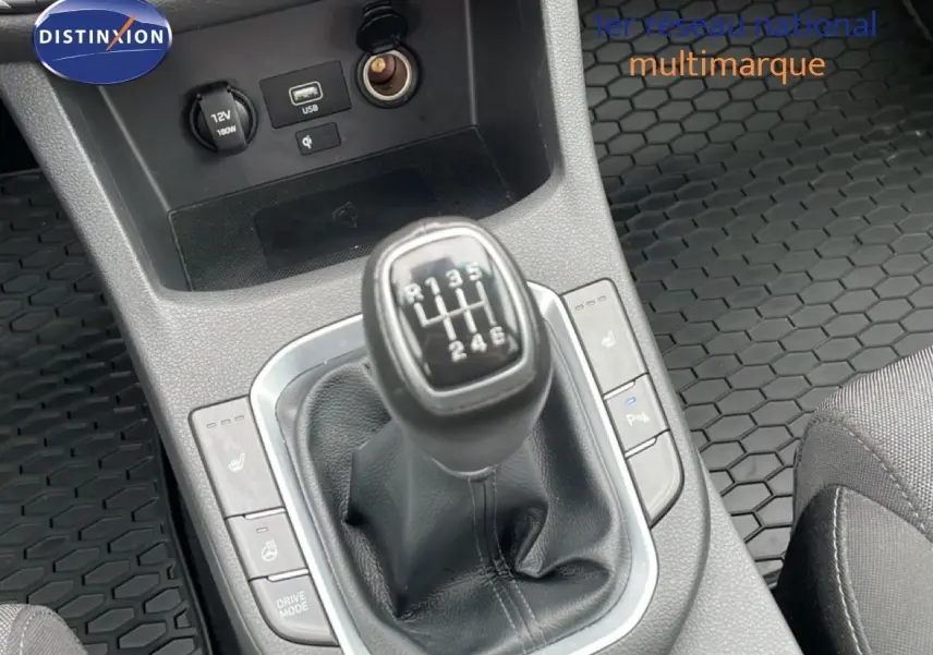Gros plan sur le levier de vitesses manuel de la Hyundai i30 SW blanche, entouré de commandes et tapis caoutchouc noir.