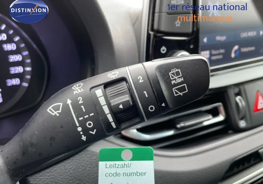 Gros plan sur la manette d’essuie-glace du tableau de bord d’une Hyundai i30 SW blanc polaire, avec affichage digital en arrière-plan.