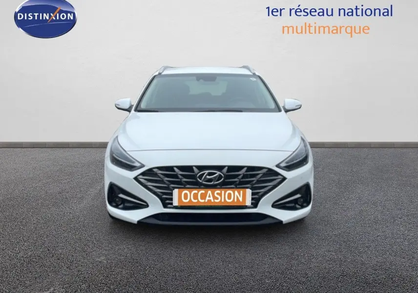 Vue frontale d'une Hyundai i30 SW blanche polaire, avec calandre noire et phares LED allumés.