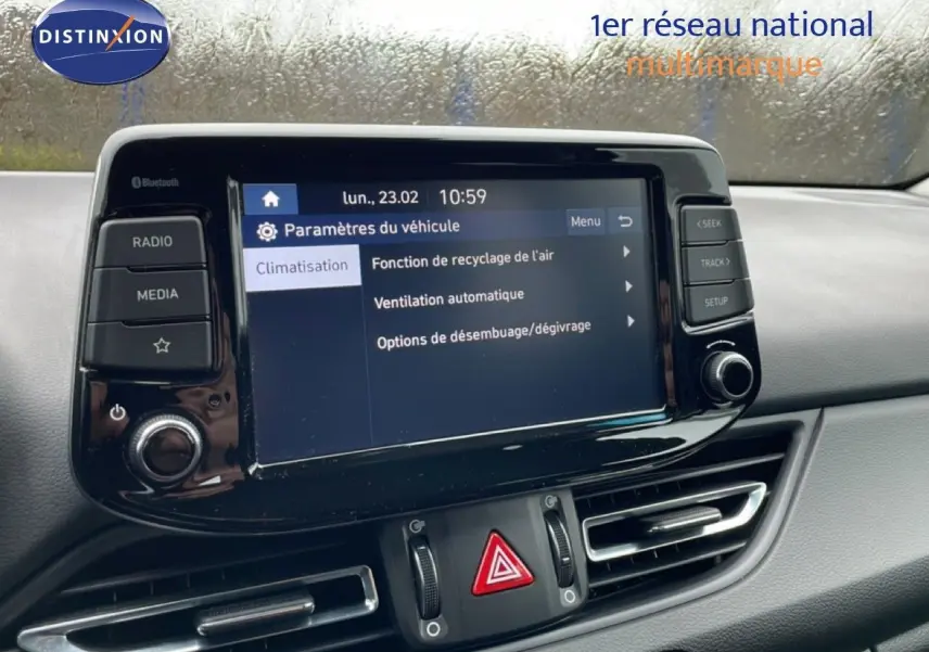 Vue intérieure centrée sur l'écran tactile du tableau de bord de la Hyundai i30 SW blanc polaire, avec commandes climatisation visibles.