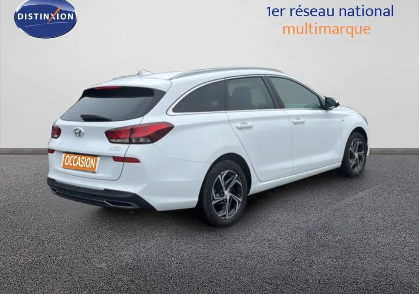 Vue 3/4 arrière droite d'une Hyundai i30 SW blanche polaire avec vitres teintées et jantes alliage noires.