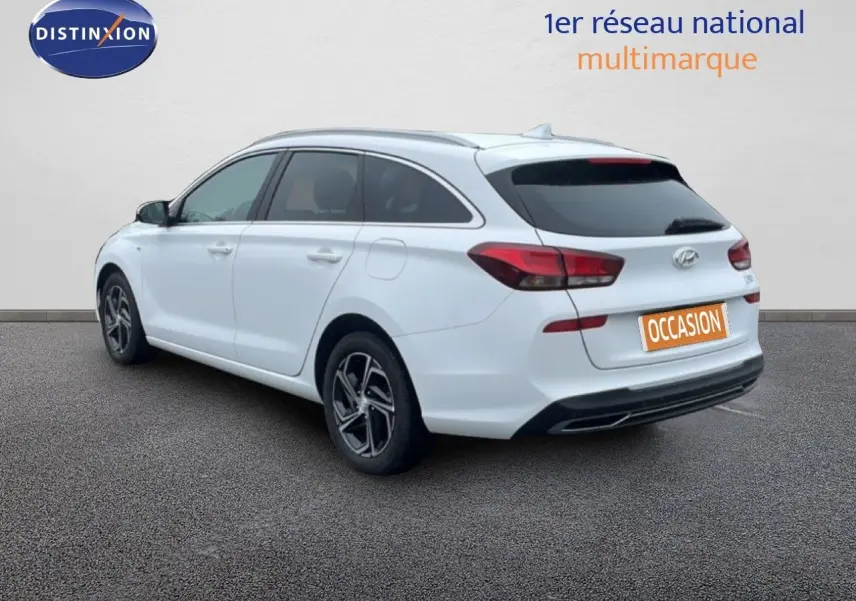 Vue 3/4 arrière droite d'une Hyundai i30 SW blanche polaire, break compact avec vitres teintées et jantes alliage.