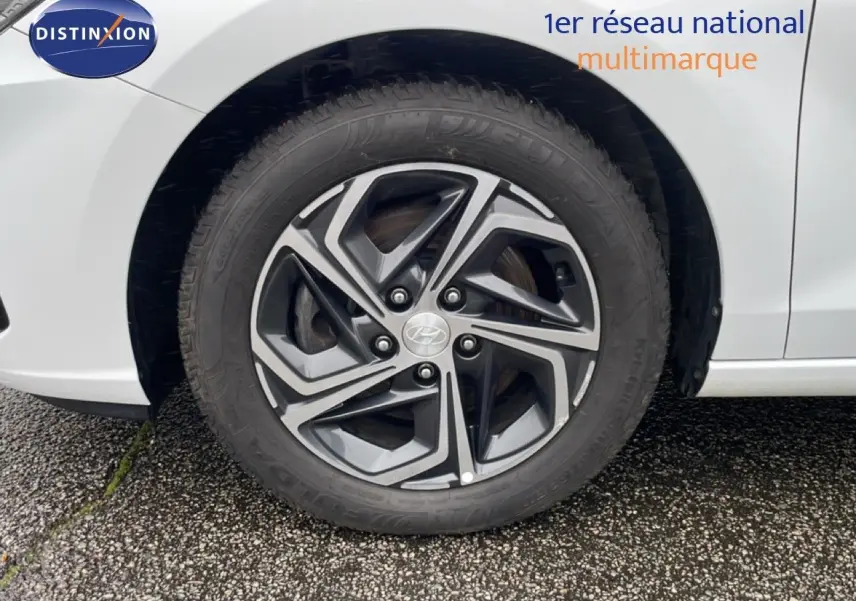 Gros plan sur la roue avant gauche d'une Hyundai i30 SW blanche polaire, mettant en valeur la jante alliage au design moderne.