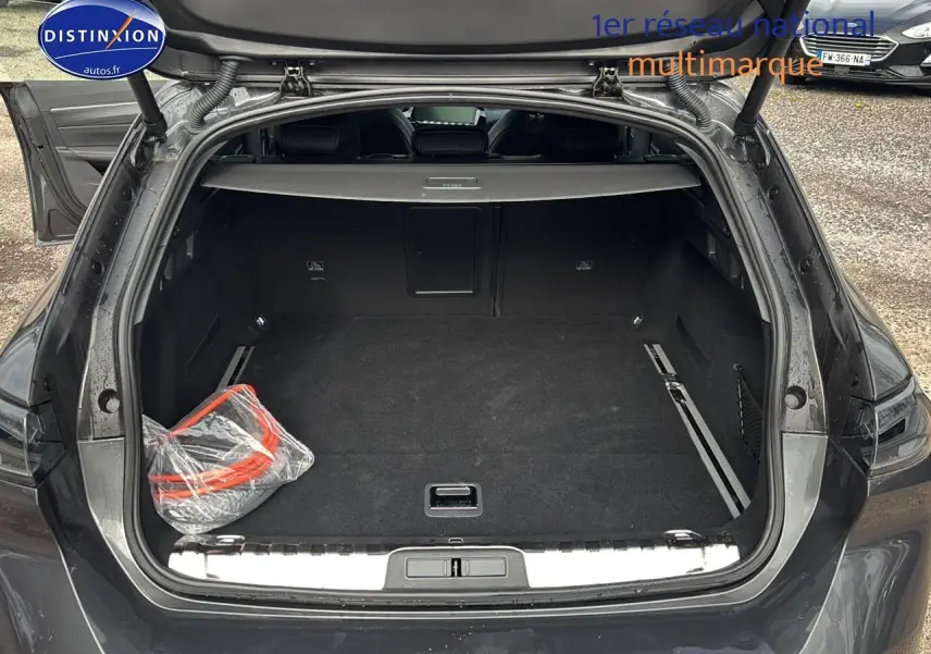 Coffre ouvert vu de l'arrière d'une Peugeot 508 SW Hybrid 225 gt e-eat8 gris titane avec tapis noir et accessoires emballés.