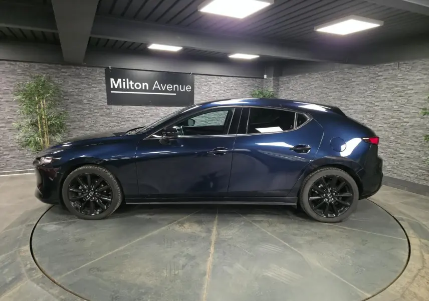Vue latérale droite d'une Mazda3 2024 bleu métallisé avec jantes alliage noires dans un showroom intérieur.