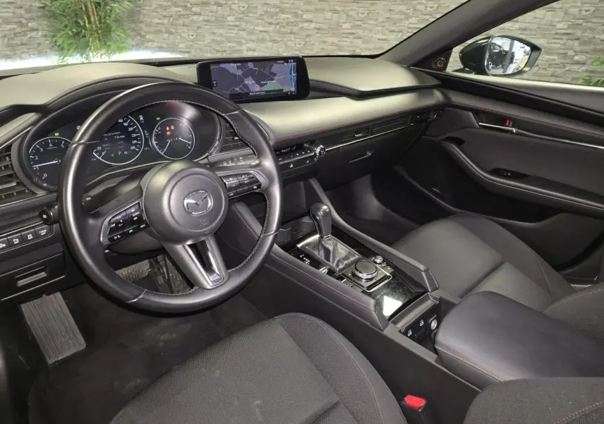 Intérieur noir de la Mazda3 2024 vu côté conducteur, avec tableau de bord moderne et écran central tactile.