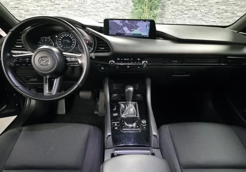 Vue intérieure avant de la Mazda3 2024, tableau de bord noir avec écran central et volant cuir multifonction.