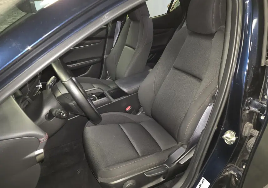 Vue intérieure côté conducteur de la Mazda3 2024 bleu, sièges tissu noir avec surpiqûres rouges et accoudoir central.