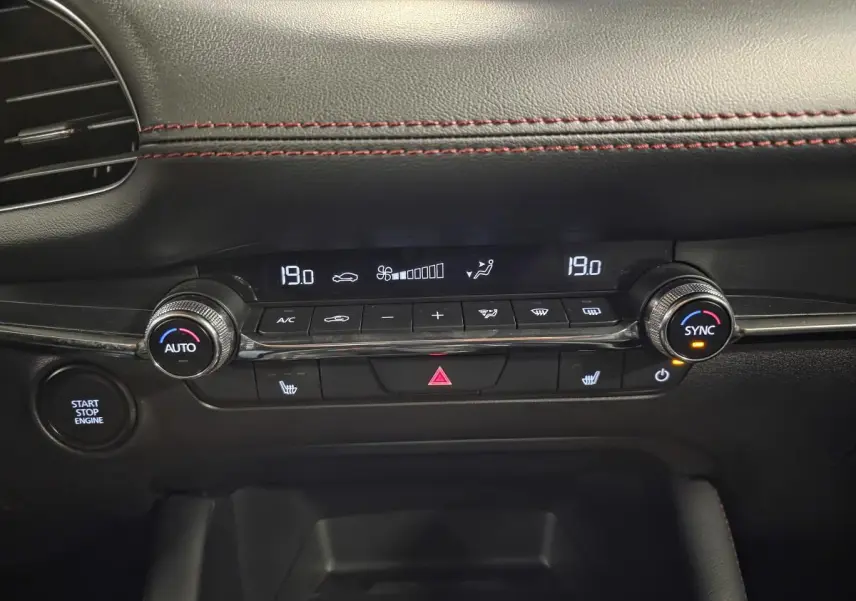Gros plan sur la console centrale noire de la Mazda3 2024, affichant la climatisation automatique et le bouton start/stop.