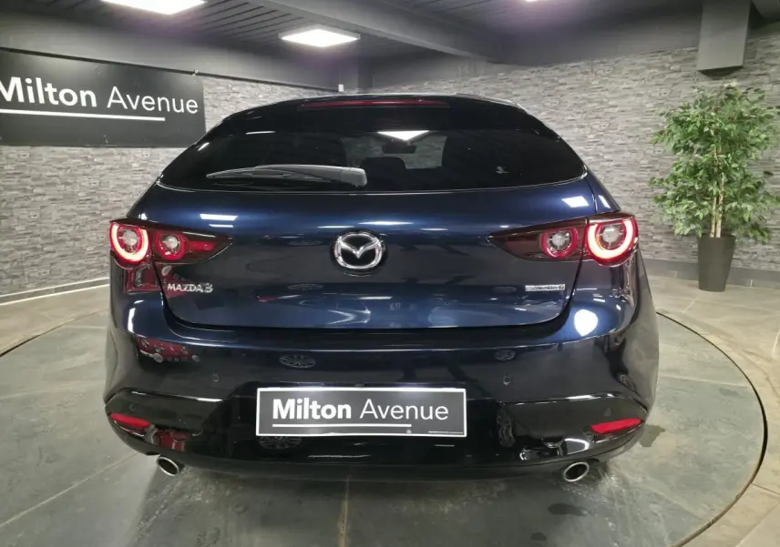 Vue arrière d'une Mazda3 bleu métallisé 2024 avec feux LED circulaires allumés dans un showroom.