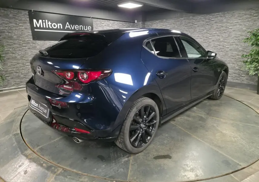 Vue 3/4 arrière droite d'une Mazda3 2024 bleu métallisé avec jantes alliage noires et becquet de toit.