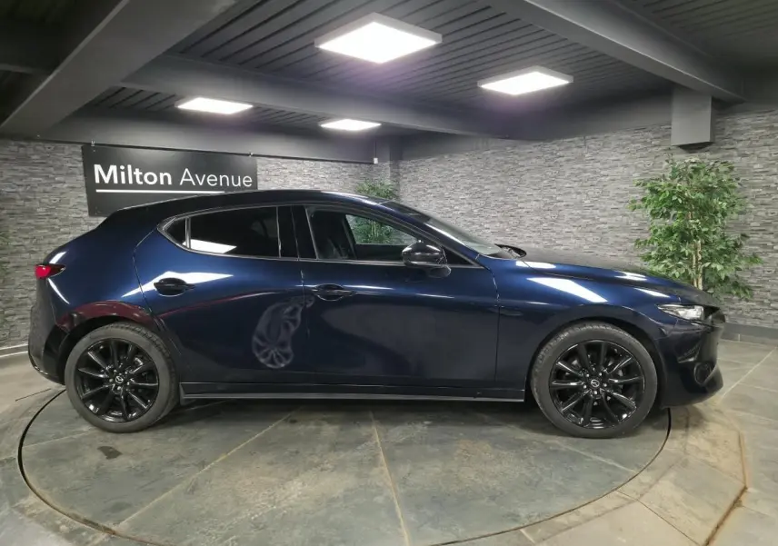 Vue latérale droite d'une Mazda3 2024 bleu métallisé avec jantes alliage noires dans un showroom.