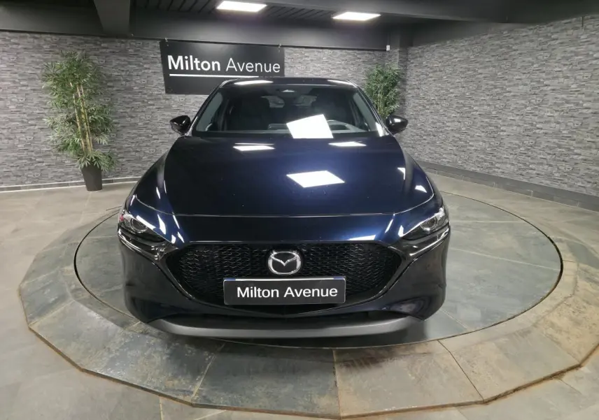 Vue frontale d'une Mazda3 2024 bleu métallisé avec calandre noire et éclairage LED dans un showroom.