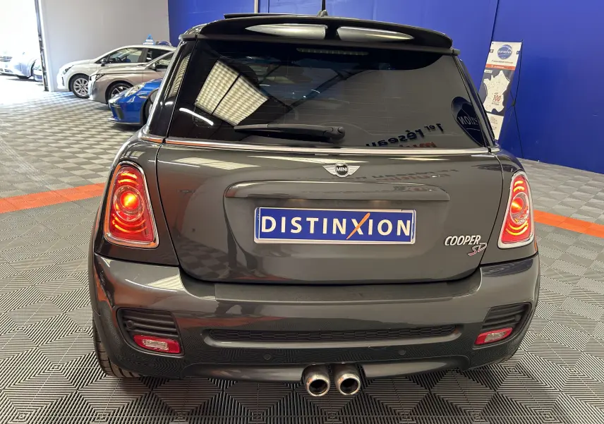 Vue arrière d'une MINI Cooper SD gris foncé avec feux allumés et double sortie d'échappement centrale dans un garage.
