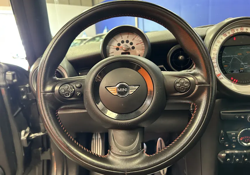 Vue centrée sur le volant noir en cuir avec coutures rouges de la MINI Cooper 2011, tableau de bord et compteur visibles.