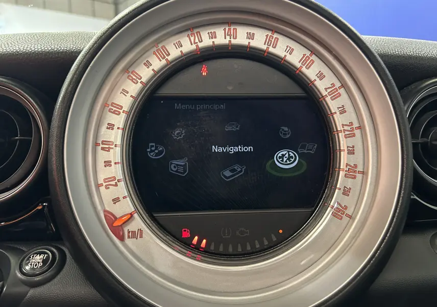 Vue rapprochée du tableau de bord de la MINI Cooper gris, affichant l'écran central de navigation et le compteur de vitesse circulaire.