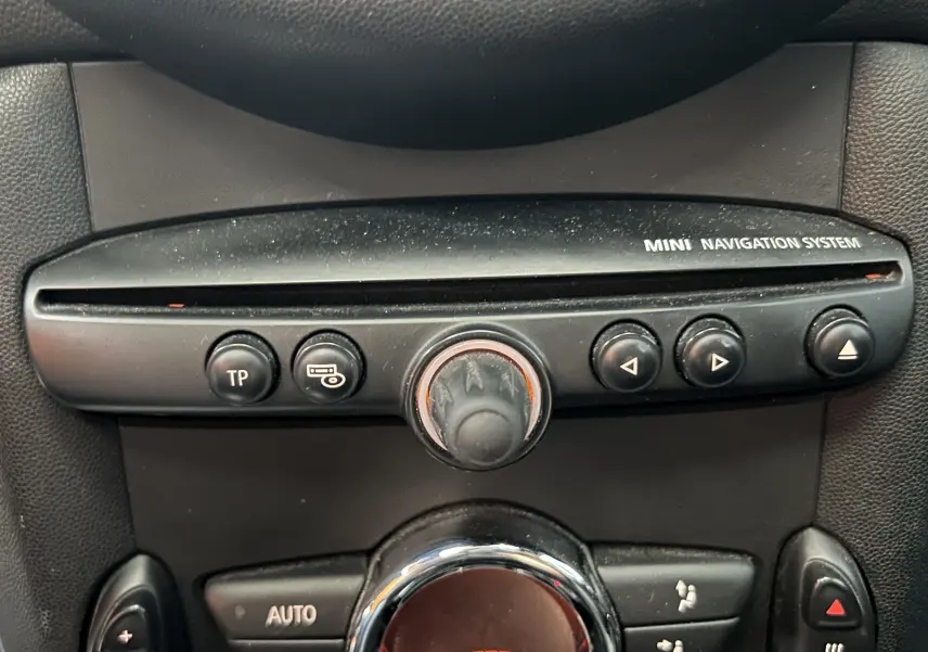 Gros plan sur la console centrale noire du MINI Cooper 2011, mettant en valeur le système de navigation et les commandes de climatisation.