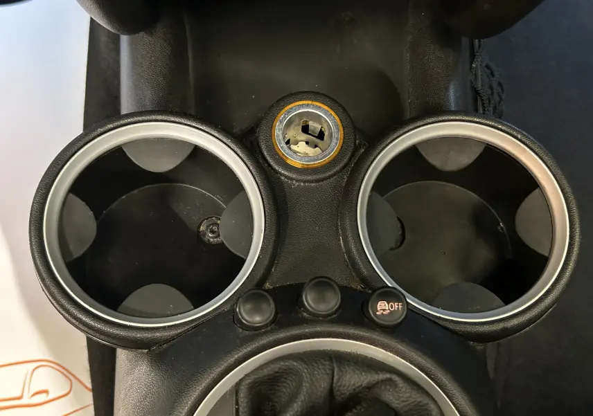 Gros plan sur la console centrale noire de la MINI Cooper 2011, montrant les porte-gobelets et un bouton de désactivation ESP.
