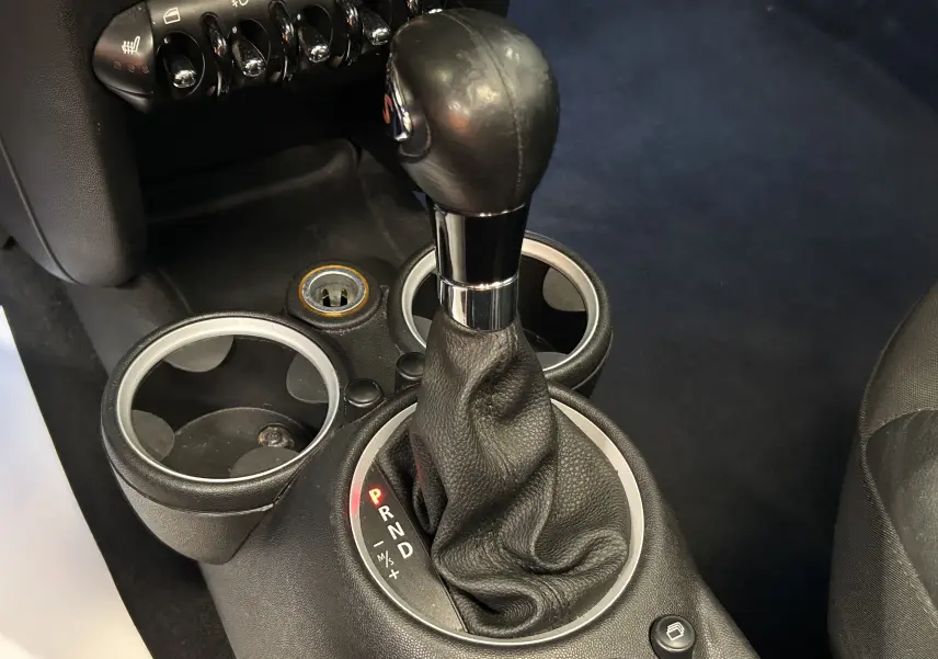 Gros plan sur le levier de vitesses automatique noir de la MINI Cooper gris, avec porte-gobelets et commandes en arrière-plan.