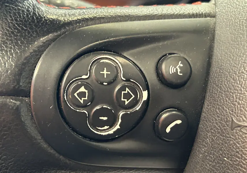 Gros plan sur les boutons de commande du volant noir d'une MINI Cooper gris, avec commandes vocales et téléphone visibles.