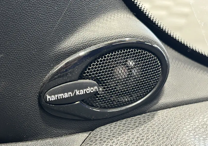 Gros plan sur l'enceinte audio Harman/Kardon intégrée dans l'habitacle noir d'une MINI Cooper gris 2011.