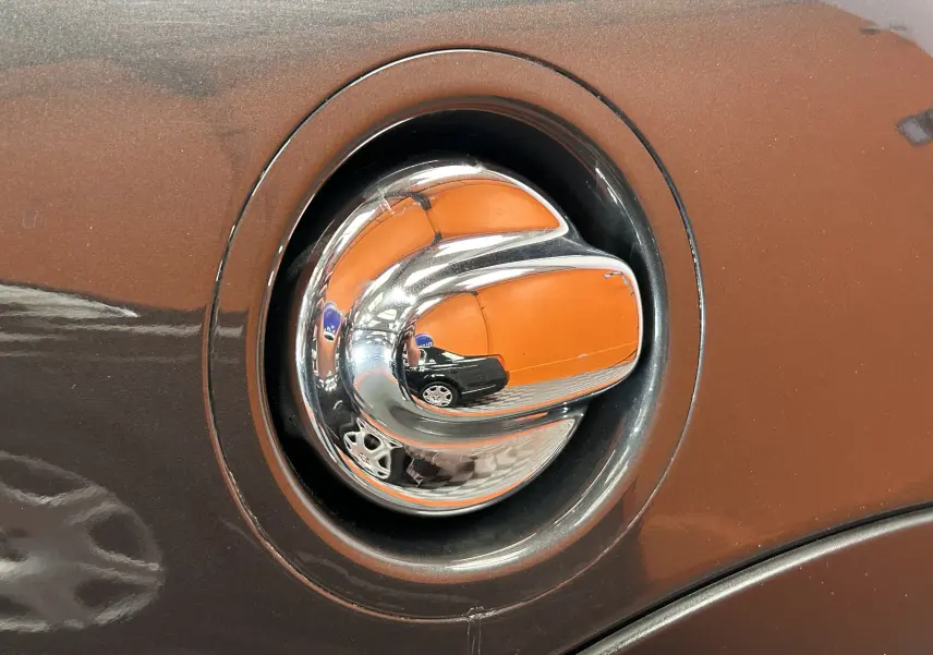 Gros plan sur la poignée de porte chromée d'une MINI Cooper gris métallisé, reflétant un mur orange en arrière-plan.