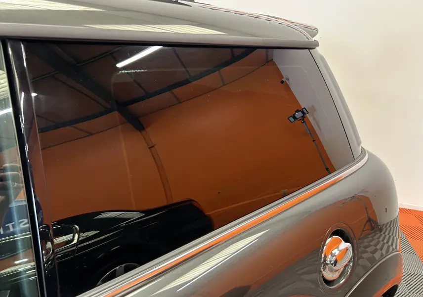 Gros plan sur la vitre arrière teintée et la carrosserie gris métallisé d'une MINI Cooper 2011 vue côté droit.
