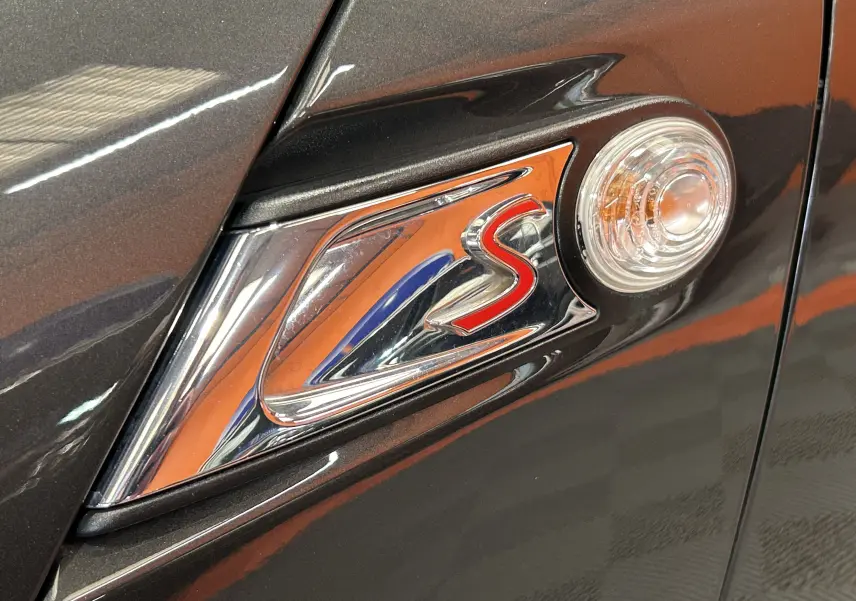 Détail du côté gauche d’une MINI Cooper gris métallisé avec logo rouge "S" et répétiteur de clignotant intégré.