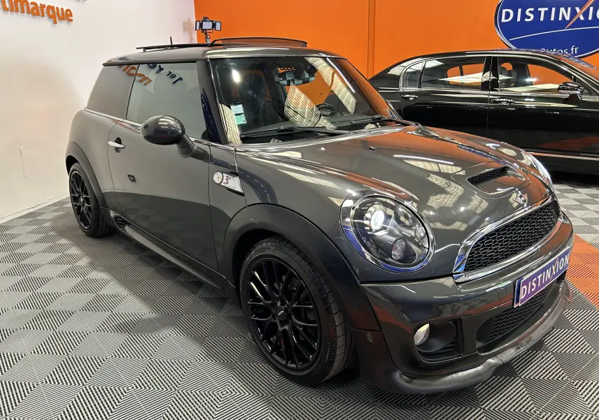 Vue 3/4 avant d'une MINI Cooper gris métallisé avec jantes noires et toit ouvrant en intérieur showroom.