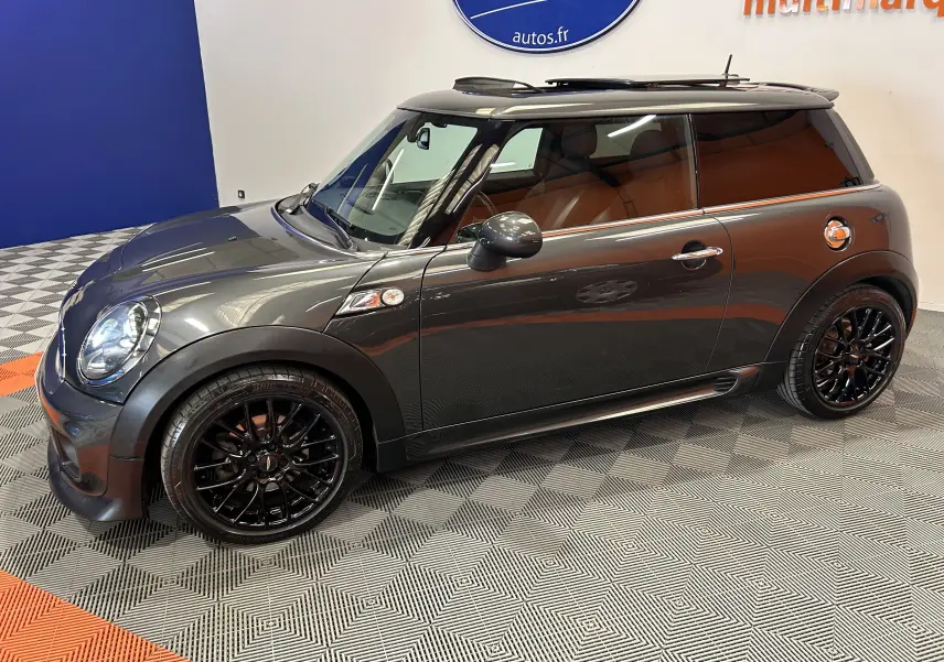 Vue latérale droite d'une MINI Cooper gris métallisé avec jantes noires et toit noir dans un showroom.