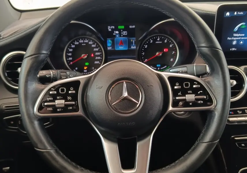 Vue rapprochée du volant cuir et aluminium d’un Mercedes GLC 300 hybride rechargeable, avec tableau de bord digital allumé.