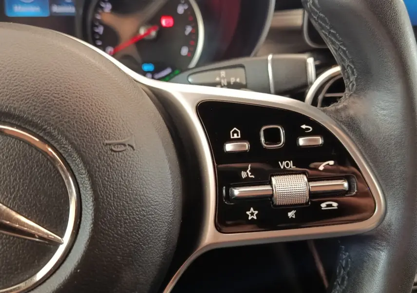 Gros plan sur les commandes de volume et fonctions vocales au volant cuir noir du Mercedes GLC 300 hybride bleu.