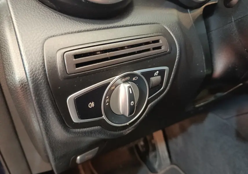 Gros plan sur la commande des phares et la sortie d'air côté gauche du tableau de bord noir d'une Mercedes GLC 300 hybride.