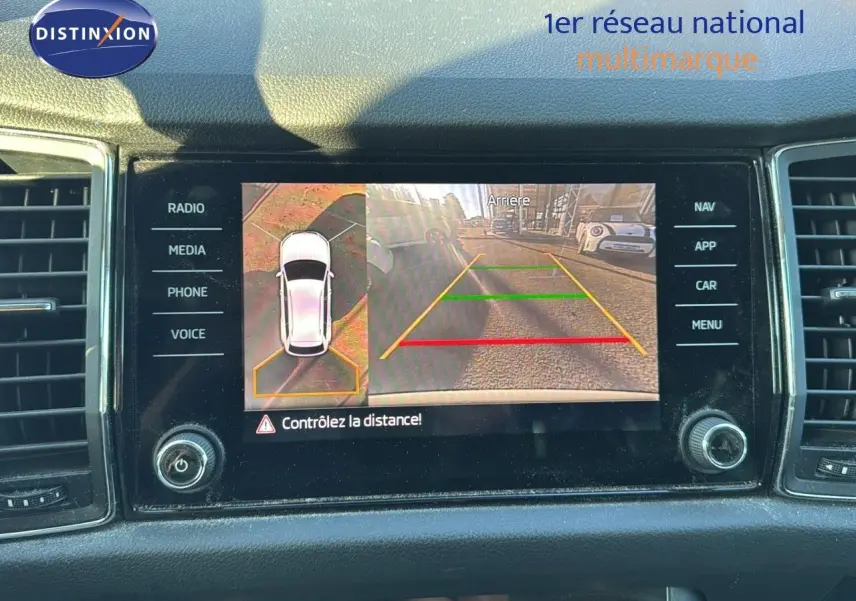 Écran central du Skoda Kodiaq blanc montrant la caméra de recul avec vue arrière et top-down du véhicule.