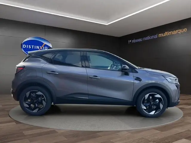 Profil droit du Renault Captur 2025 gris Cassiopée avec toit noir, roues noires et peinture bi-ton, en intérieur showroom.
