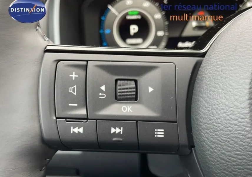 Gros plan sur les commandes gauche du volant cuir gris du Nissan Qashqai 2025 avec affichage numérique en arrière-plan.