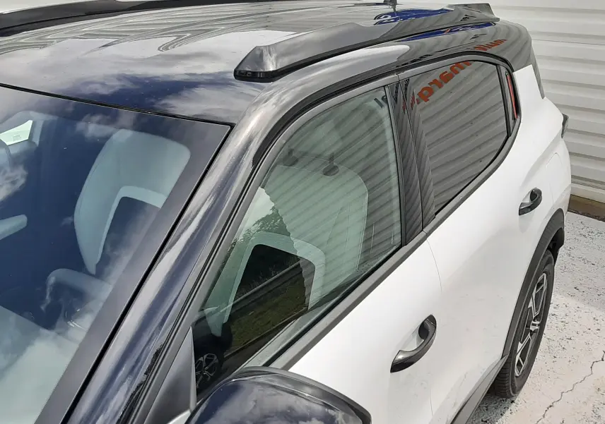 Vue côté gauche en léger plongé d'un Citroën C3 Aircross 2026 blanc banquise avec toit et rétroviseur noir brillant.